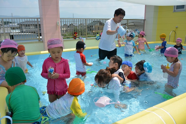 園児たちがプールで水鉄砲やじょうろなどで遊んでいる写真